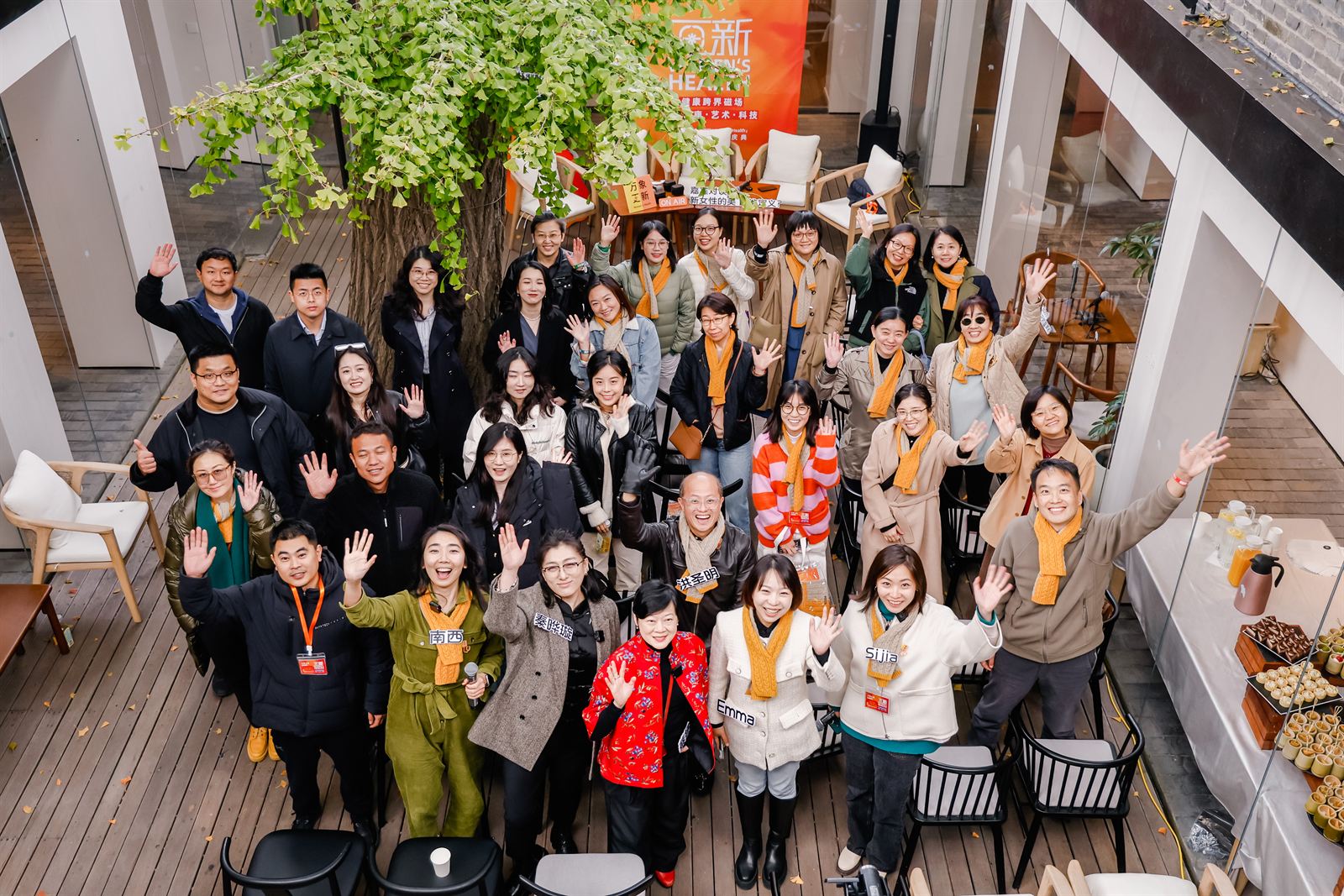 A large group gathered under a ginkgo tree in a Beijing courtyard at the 亘新 women's-health programme, photographed from above